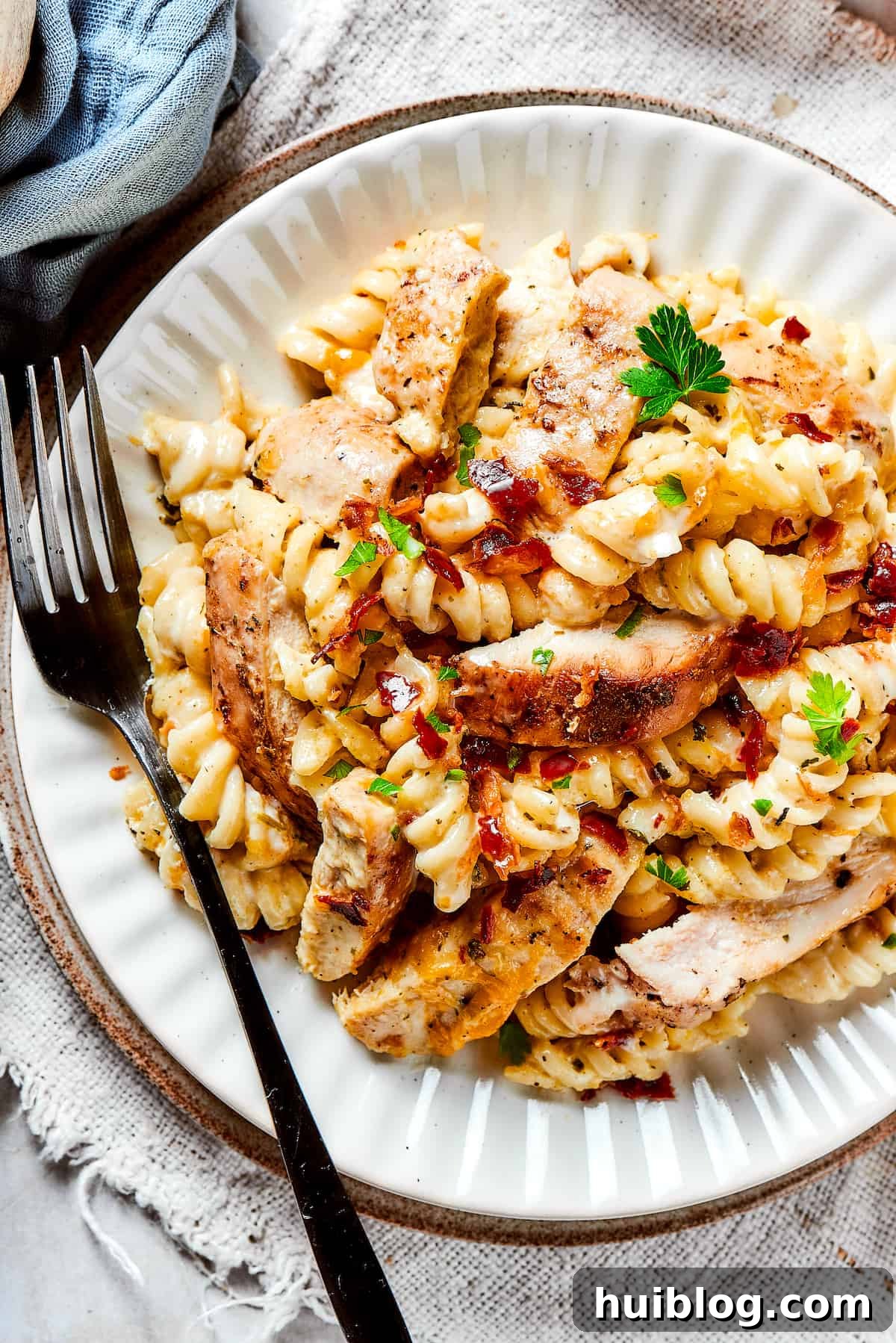 Creamy Chicken Bacon Ranch Pasta: A savory, smoky dinner bursting with flavor! A dinner plate of pasta and chicken with creamy sauce and bacon, garnished with fresh parsley.