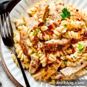 A dinner plate of pasta and chicken with creamy sauce and bacon, garnished with fresh parsley.