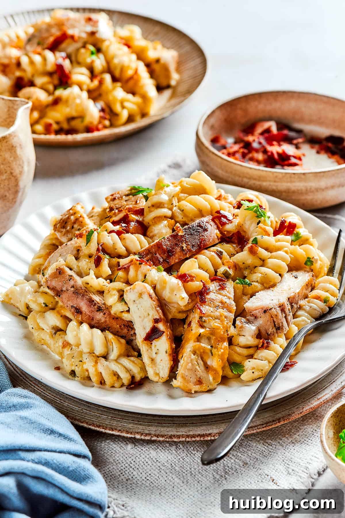 This bold and creamy Chicken Bacon Ranch Pasta recipe is a savory, smoky dinner dish that's bursting with flavor! The best comfort food! Plates of creamy chicken pasta garnished with fresh parsley.