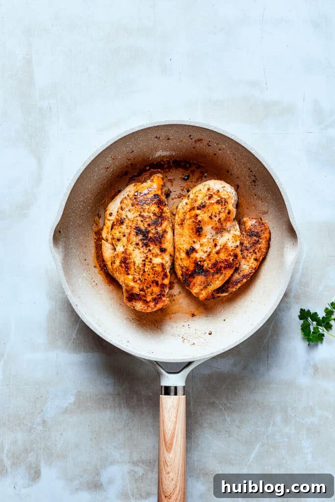 Cooking chicken to golden perfection in bacon fat. Sizzling chicken breasts cooking in a skillet with bacon fat, developing a golden crust.