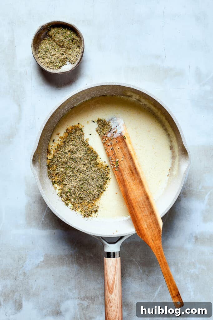 Perfecting the creamy sauce base for the pasta. Close-up view of a skillet filled with a creamy white sauce, simmering gently and thickening.