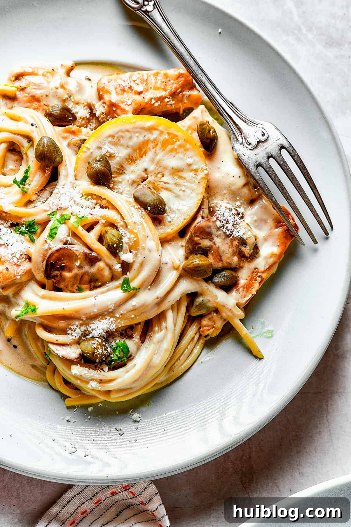 This chef’s-kiss-perfect Chicken Piccata Cheesecake Factory Copycat is loaded with juicy chicken, mushrooms, and pasta in a creamy sauce. Overhead view of a generous helping of chicken pasta on a dinner plate with a fork.