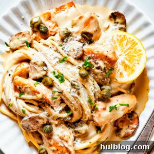 Chicken in caper-lemon sauce with pasta on a pale dinner plate.