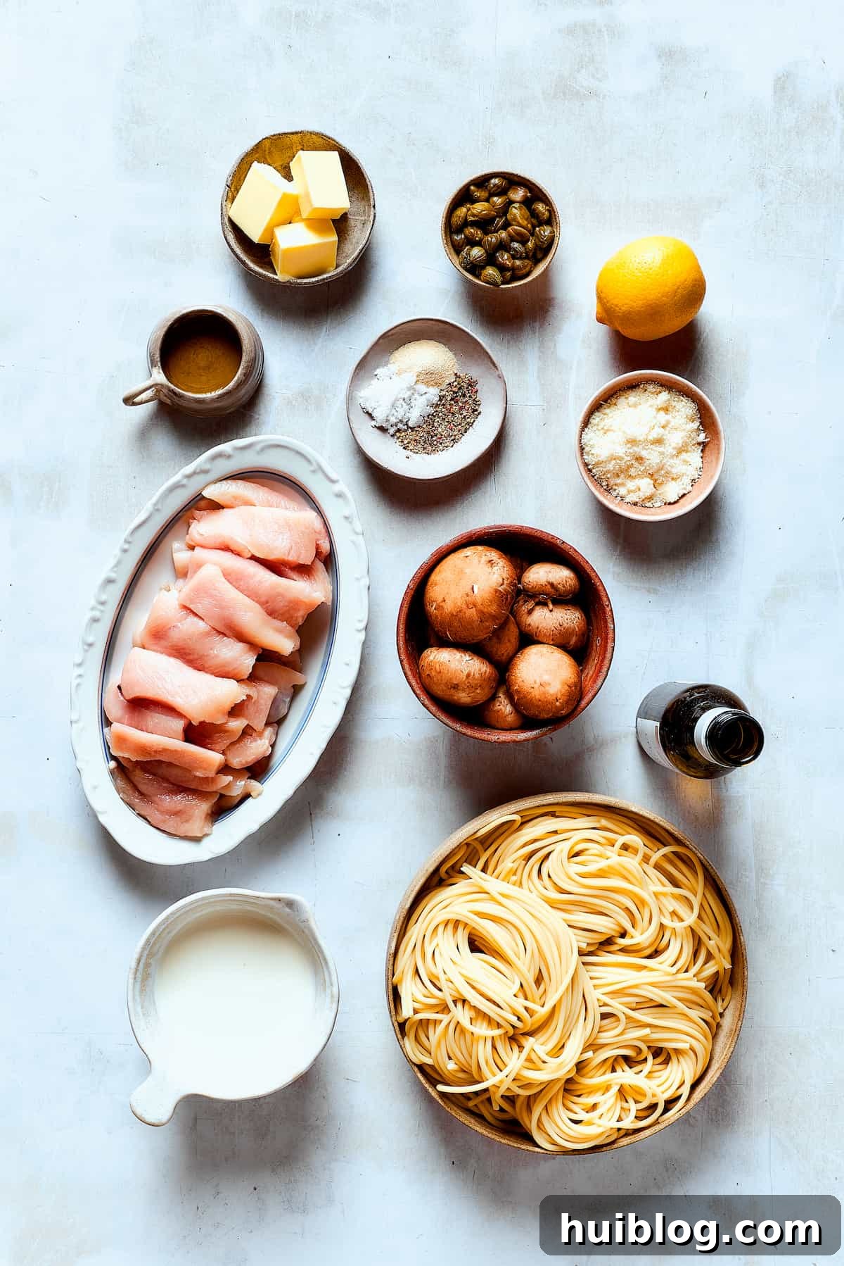 This chef’s-kiss-perfect Chicken Piccata Cheesecake Factory Copycat is loaded with juicy chicken, mushrooms, and pasta in a creamy sauce. Ingredients for a chicken piccata cheesecake factory copycat, arranged on a work surface.