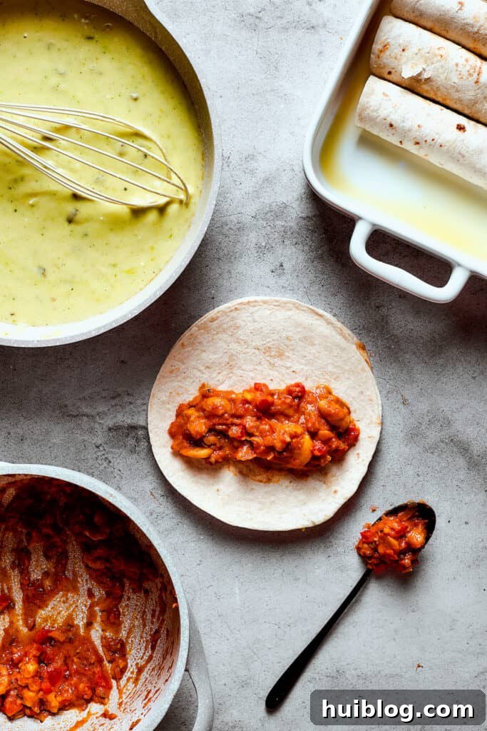 Shrimp Enchiladas are an easy, cheesy dinner with chopped shrimp and green enchilada sauce. The perfect balance of creamy, spicy, and savory! A baking dish with enchiladas in it. One tortilla is on the work surface with shrimp filling arranged down the center.