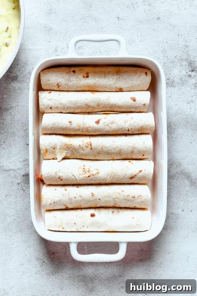 Shrimp Enchiladas are an easy, cheesy dinner with chopped shrimp and green enchilada sauce. The perfect balance of creamy, spicy, and savory! A baking dish full of rolled-up enchiladas.