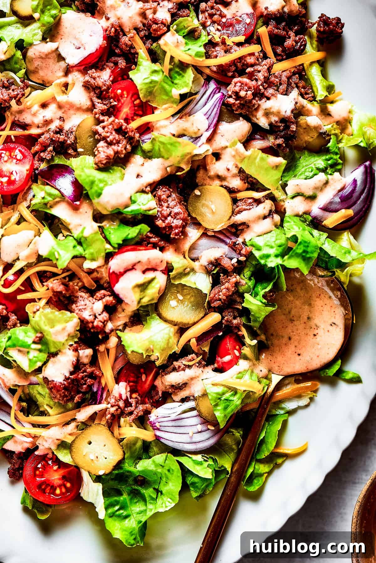 Close-up of a Big Mac Salad with red onion, ground beef, shredded cheese, and more.