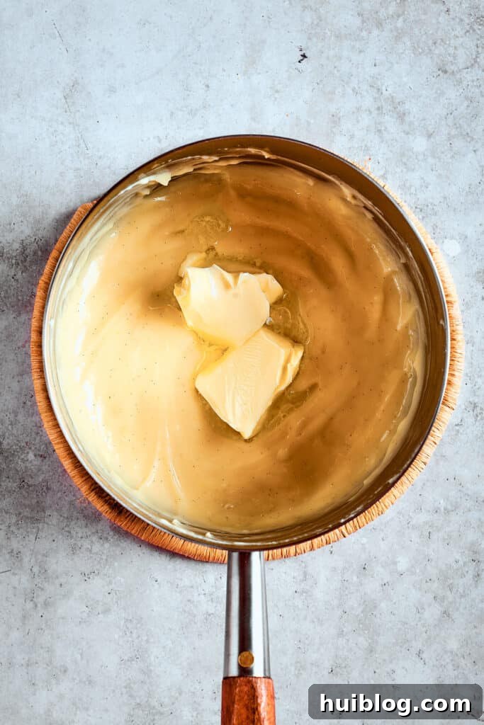 Adding butter for ultimate creaminess. Unsalted butter being stirred into the warm, freshly made banana pudding, adding a rich, velvety finish.
