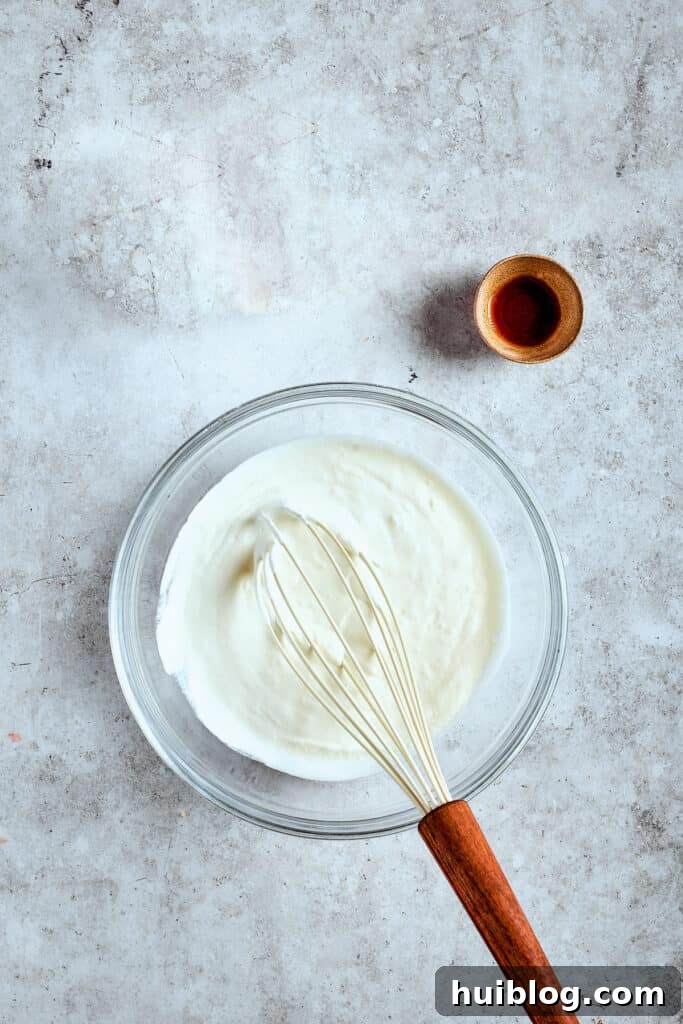 Whipping cream to light, airy perfection. Heavy whipping cream being whipped with vanilla extract in a mixer, forming soft peaks for the fluffy topping.