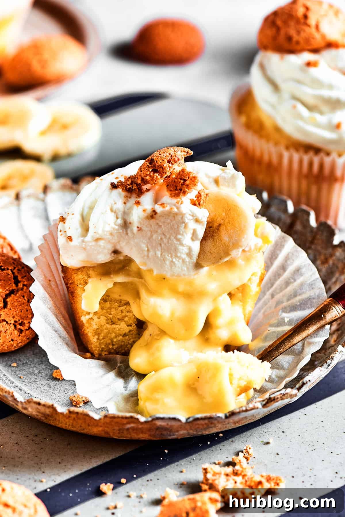 Discover the delightful secret: A creamy banana pudding core nestled within each cupcake! A half-eaten banana pudding cupcake with its wrapper pulled down, revealing the generous and creamy banana pudding filling spilling out, highlighting its decadent center.