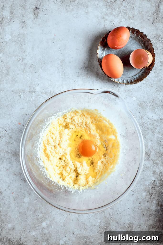 Adding eggs precisely for a perfect cupcake batter. Eggs being added one by one to the creamed butter and sugar mixture, ensuring each is fully incorporated before the next addition.