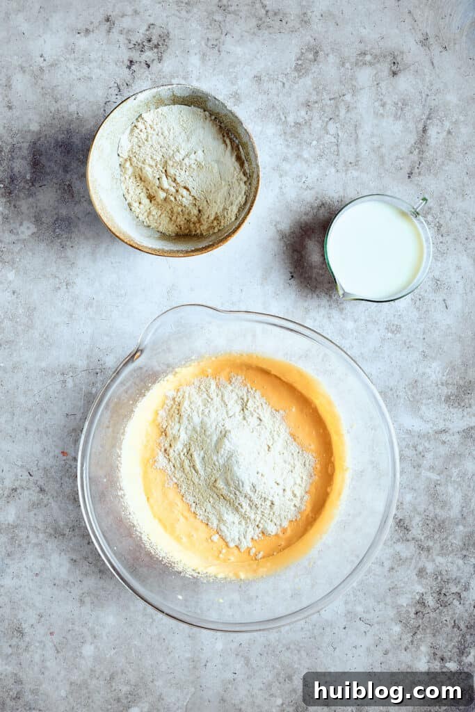 Careful mixing is key to a tender cupcake crumb. The dry ingredients are being gradually added to the wet batter, alternating with milk, to create a smooth cupcake mixture.