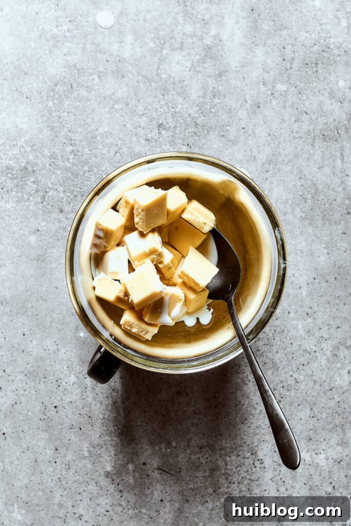 White chocolate chunks and heavy cream being gently melted together in a microwave-safe bowl to create a smooth ganache.