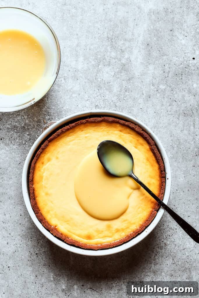Smooth white chocolate ganache being spread meticulously over the top of a chilled cheesecake, creating an even layer.