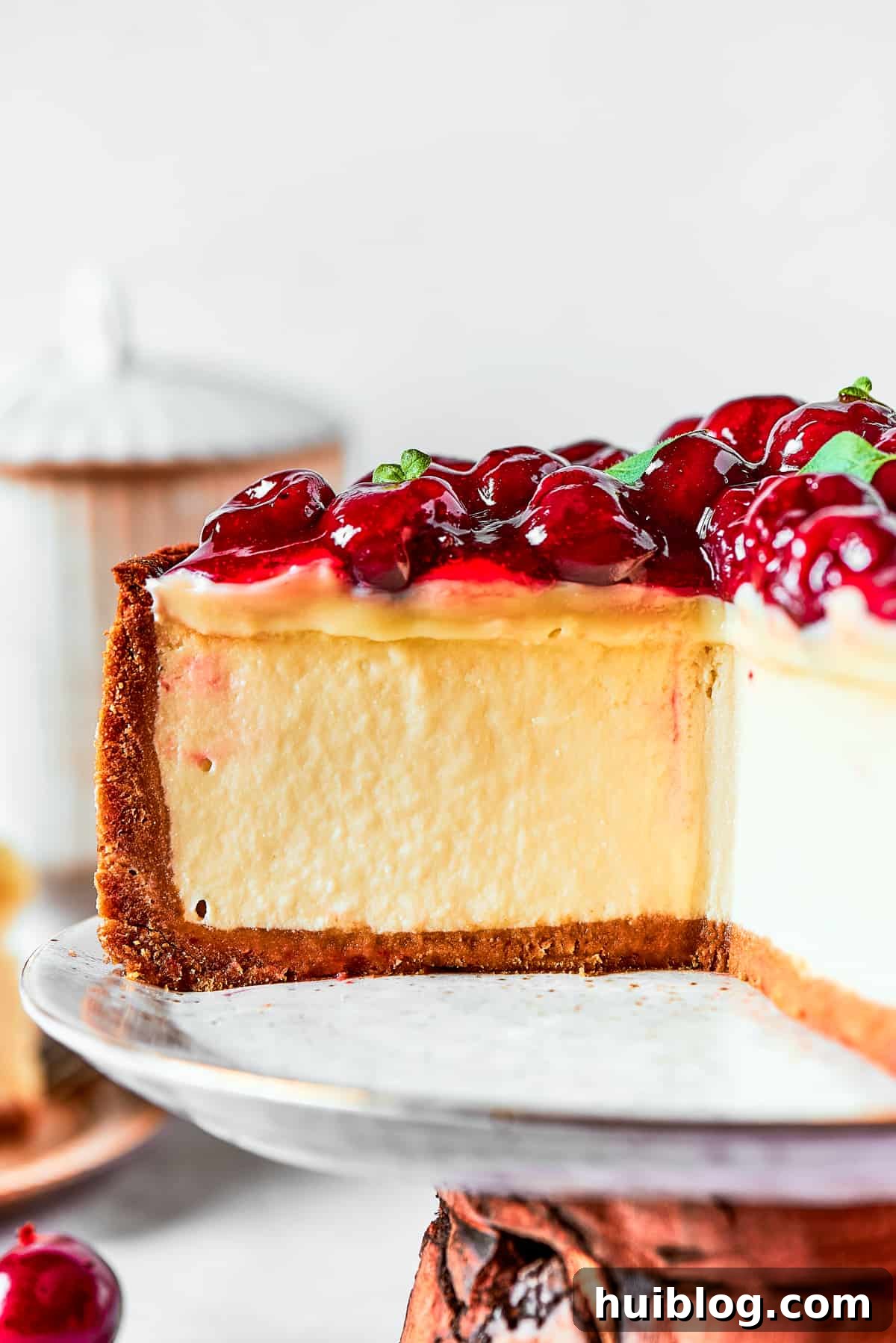 A stunning Cherry Cheesecake, topped generously with bright red cherries and white chocolate ganache, proudly displayed on a decorative cake stand.