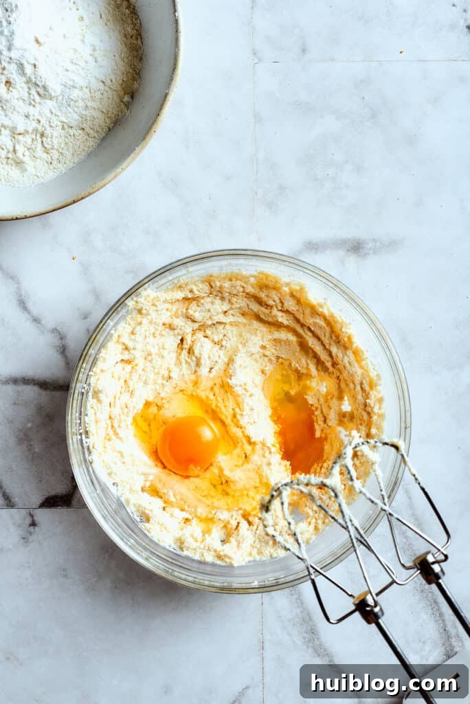 Lemon cookies are tender, soft, moist, and chewy, with tart and tangy fresh lemon flavor balanced by rich brown sugar and smooth vanilla. Overhead view of a mixing bowl with creamed butter and two eggs on top, with beaters.