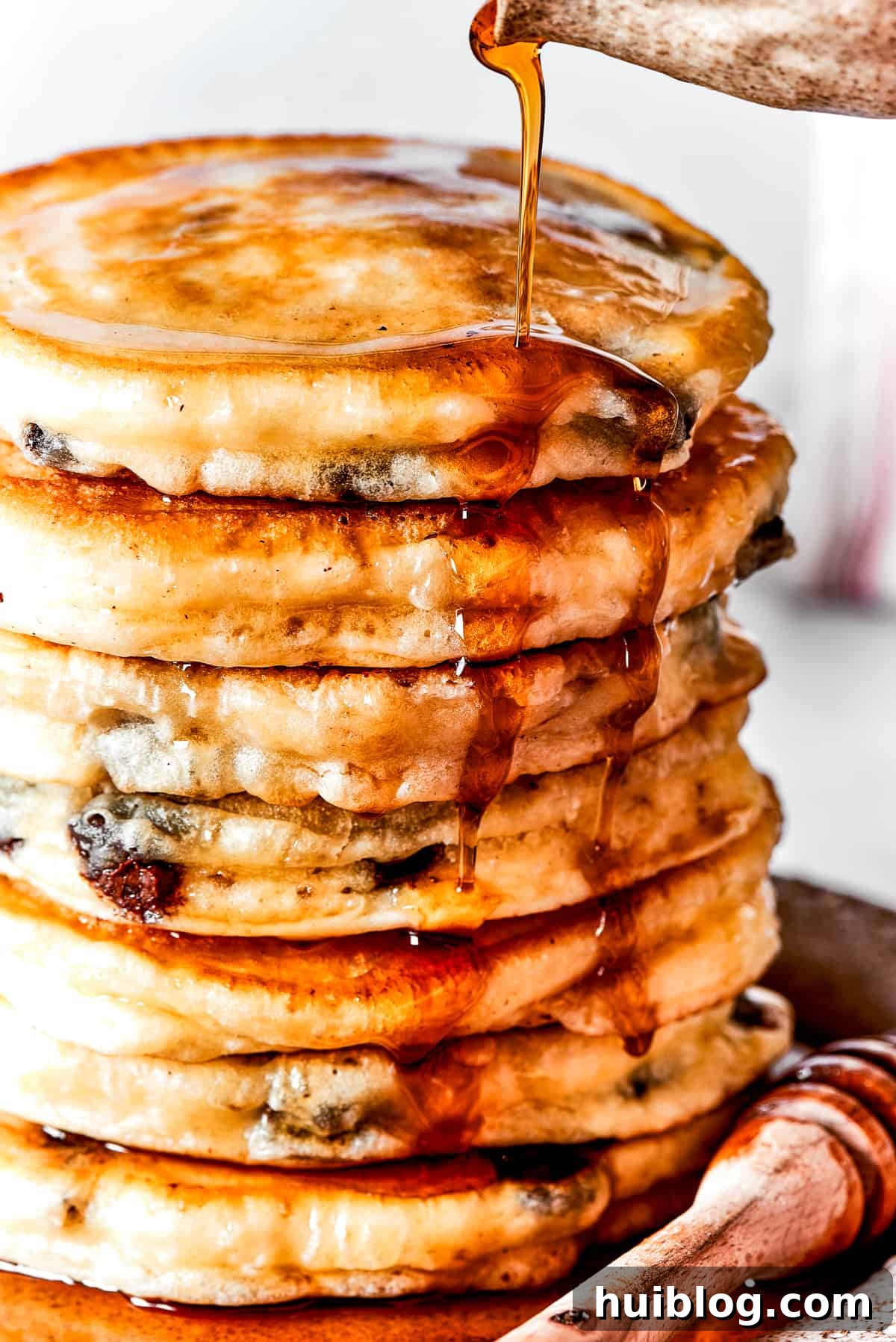 Pouring maple syrup over a stack of fluffy chocolate chip pancakes.