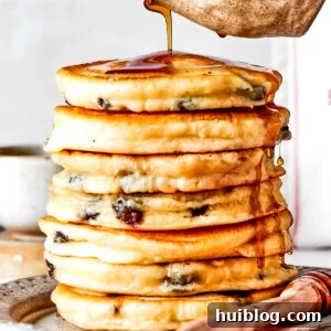Pouring maple syrup over a stack of chocolate chip pancakes.