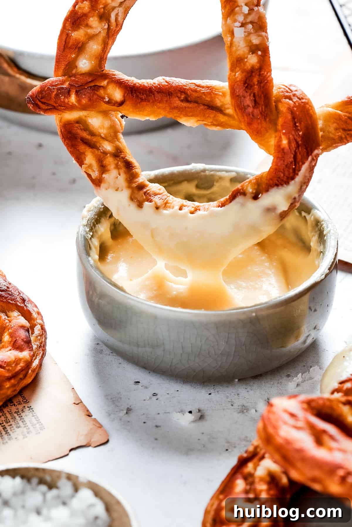 A freshly baked soft pretzel is being dipped into a luscious, golden cheese sauce, showcasing the perfect snack combination.