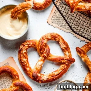 Baked soft pretzels are shown on a rack with cheese sauce alongside.