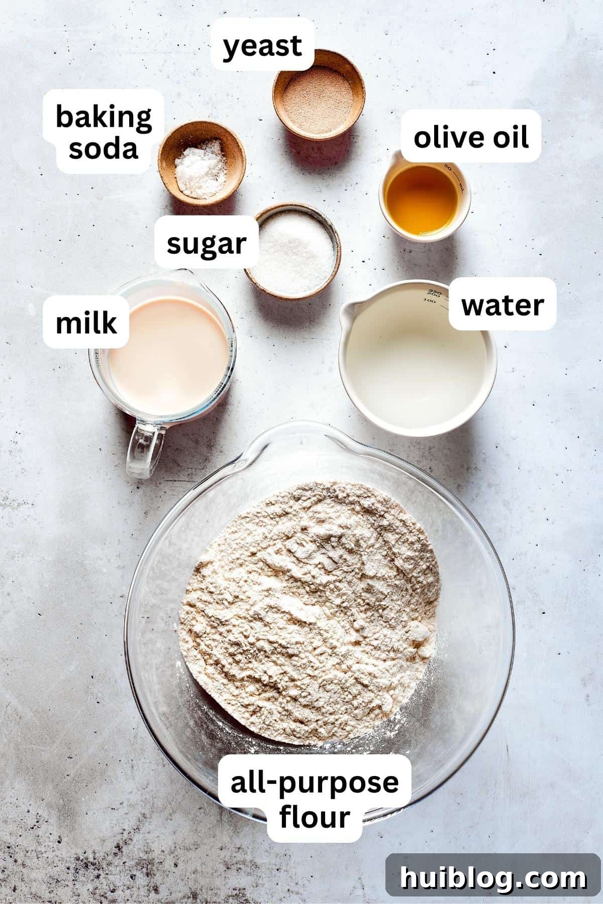 Ingredients for soft pretzels are shown portioned out into bowls: flour, yeast, sugar, milk, butter, and water, ready for mixing.