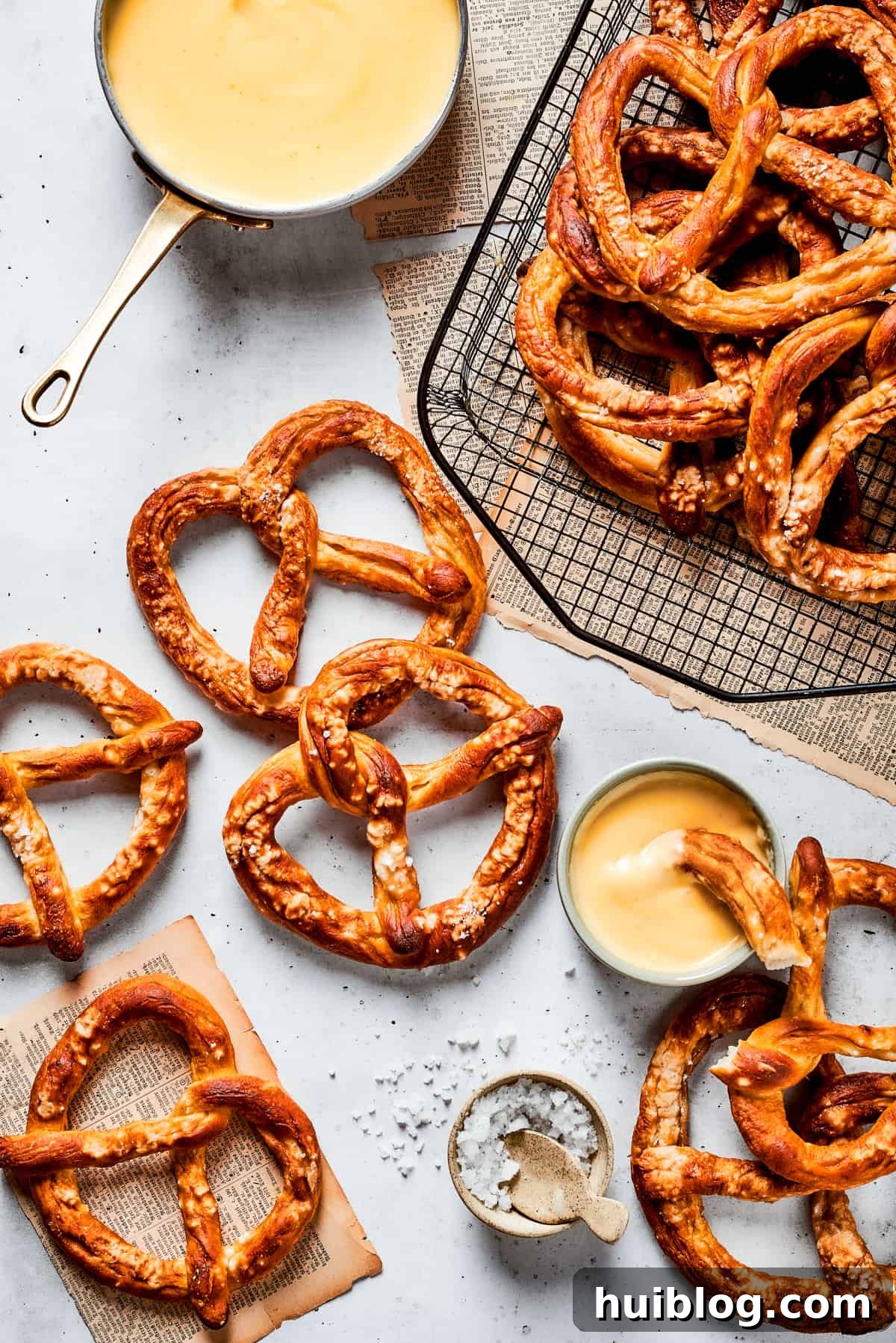 Baked soft pretzels are arranged on a wire rack, with a bowl of creamy, golden cheese sauce alongside, ready for dipping.