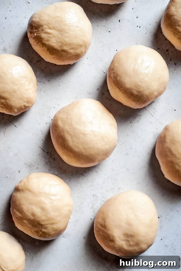 Small, uniformly sized balls of soft pretzel dough are neatly arranged on a white surface, ready for shaping.