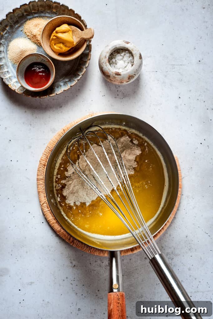 A metal whisk stirs a creamy, golden cheese sauce in a saucepan over gentle heat, showing the smooth texture of the dip.