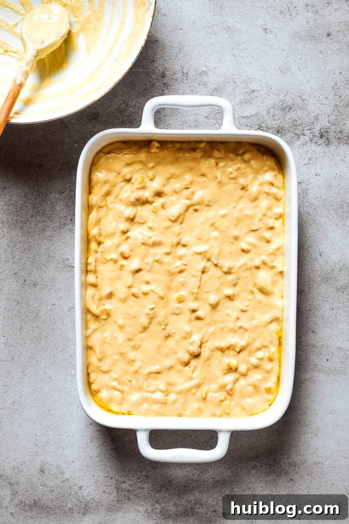The smooth, creamy corn souffle batter is shown in a white baking pan, ready to be placed in the oven for baking.