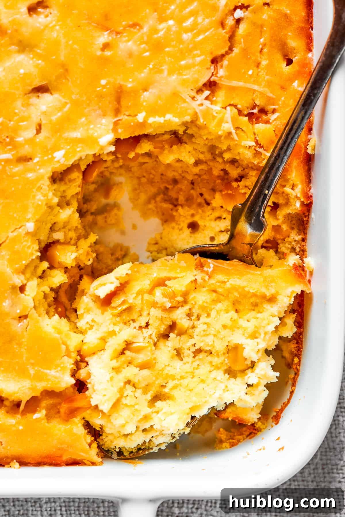 Close up image of a spoon taking out a large, creamy bite of corn souffle, highlighting its perfect texture and golden crust.