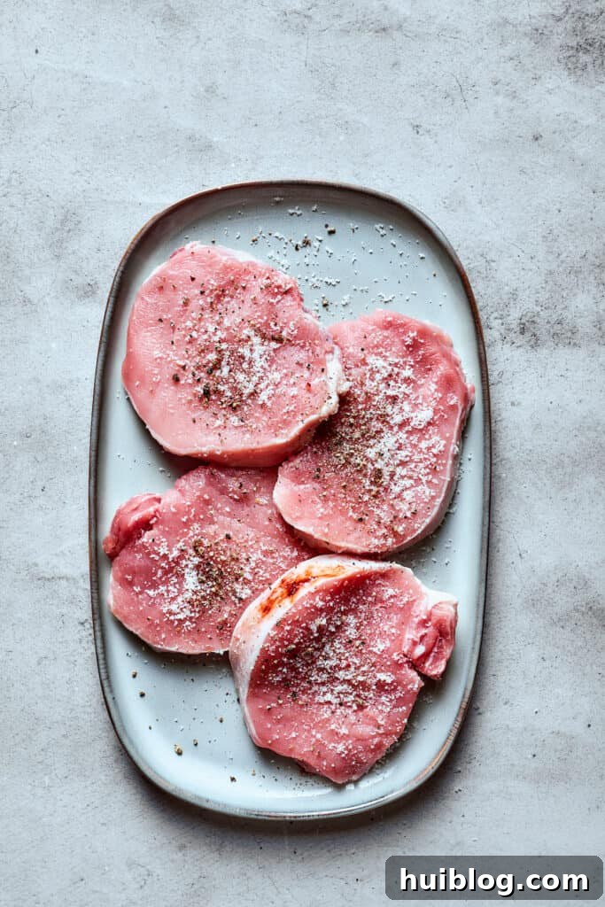 These Honey Garlic Pork Chops are the perfect blend of sweet-salty with a punch of extra flavor from minced garlic. Ready in 20 minutes! Boneless pork chops seasoned generously with sea salt and freshly ground black pepper, laid out on a clean white tray, ready for searing.