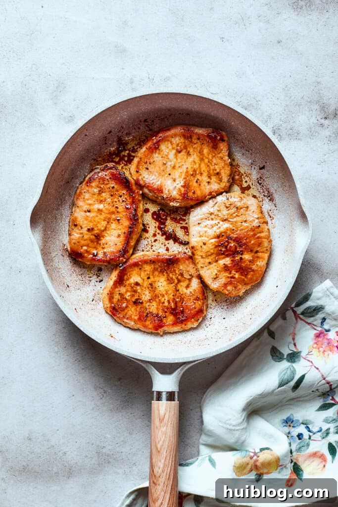 These Honey Garlic Pork Chops are the perfect blend of sweet-salty with a punch of extra flavor from minced garlic. Ready in 20 minutes! Two boneless pork chops searing beautifully in a hot white skillet, their edges turning golden brown and developing a delicious crust.
