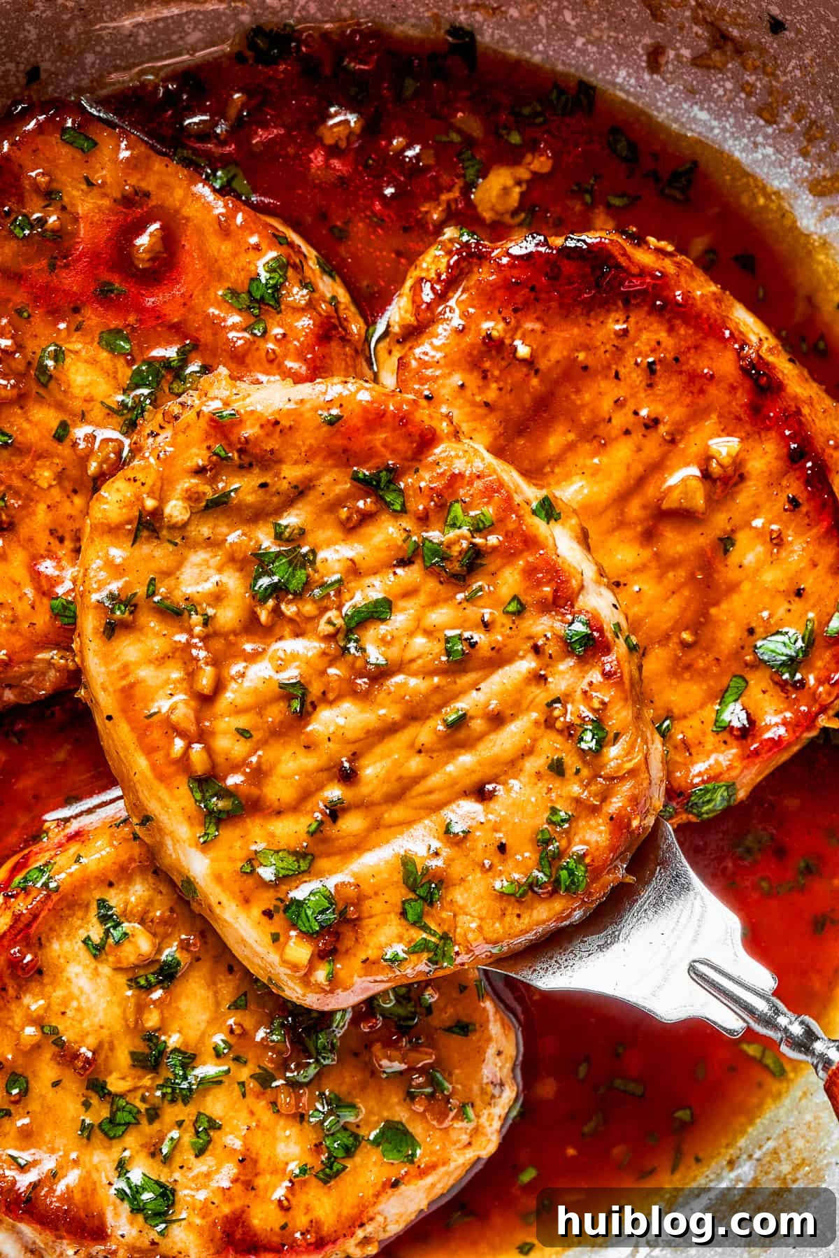 These Honey Garlic Pork Chops are the perfect blend of sweet-salty with a punch of extra flavor from minced garlic. Ready in 20 minutes! An inviting close-up of finished honey garlic pork chops, glistening with their sweet and savory sauce, garnished with fresh green parsley.