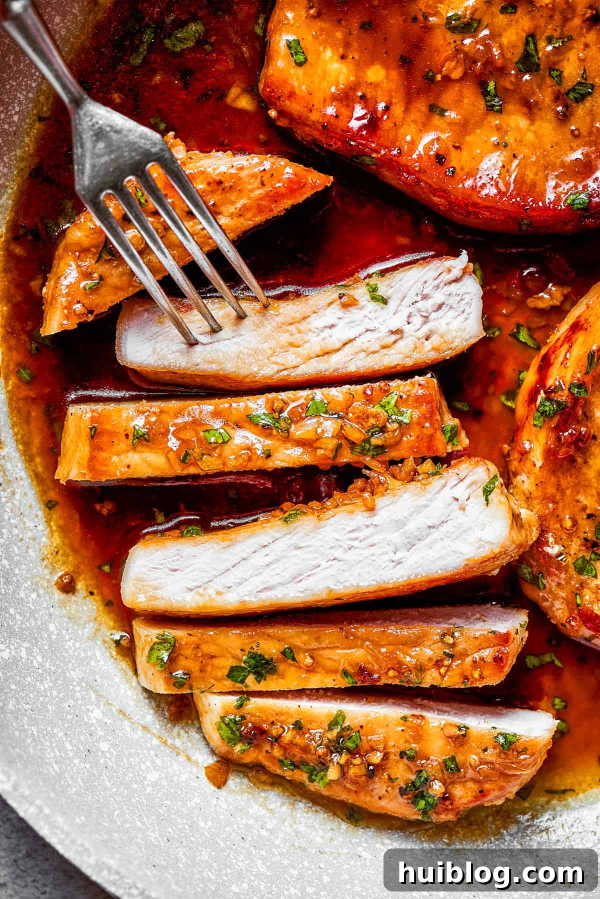 These Honey Garlic Pork Chops are the perfect blend of sweet-salty with a punch of extra flavor from minced garlic. Ready in 20 minutes! Expertly sliced honey garlic pork chops arranged on a white plate, with a fork poised to pick up a tender, sauce-coated piece.