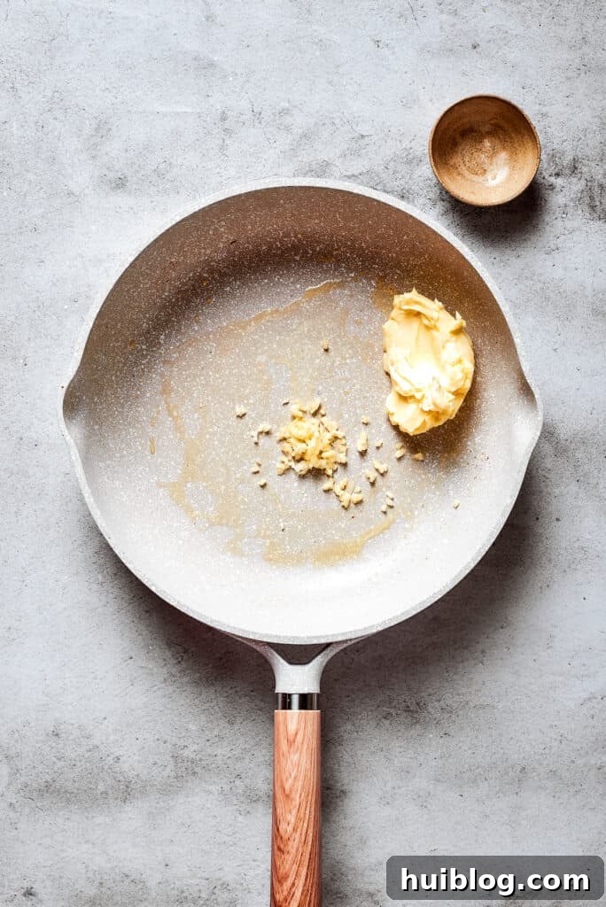 A white skillet holds butter and chopped garlic.