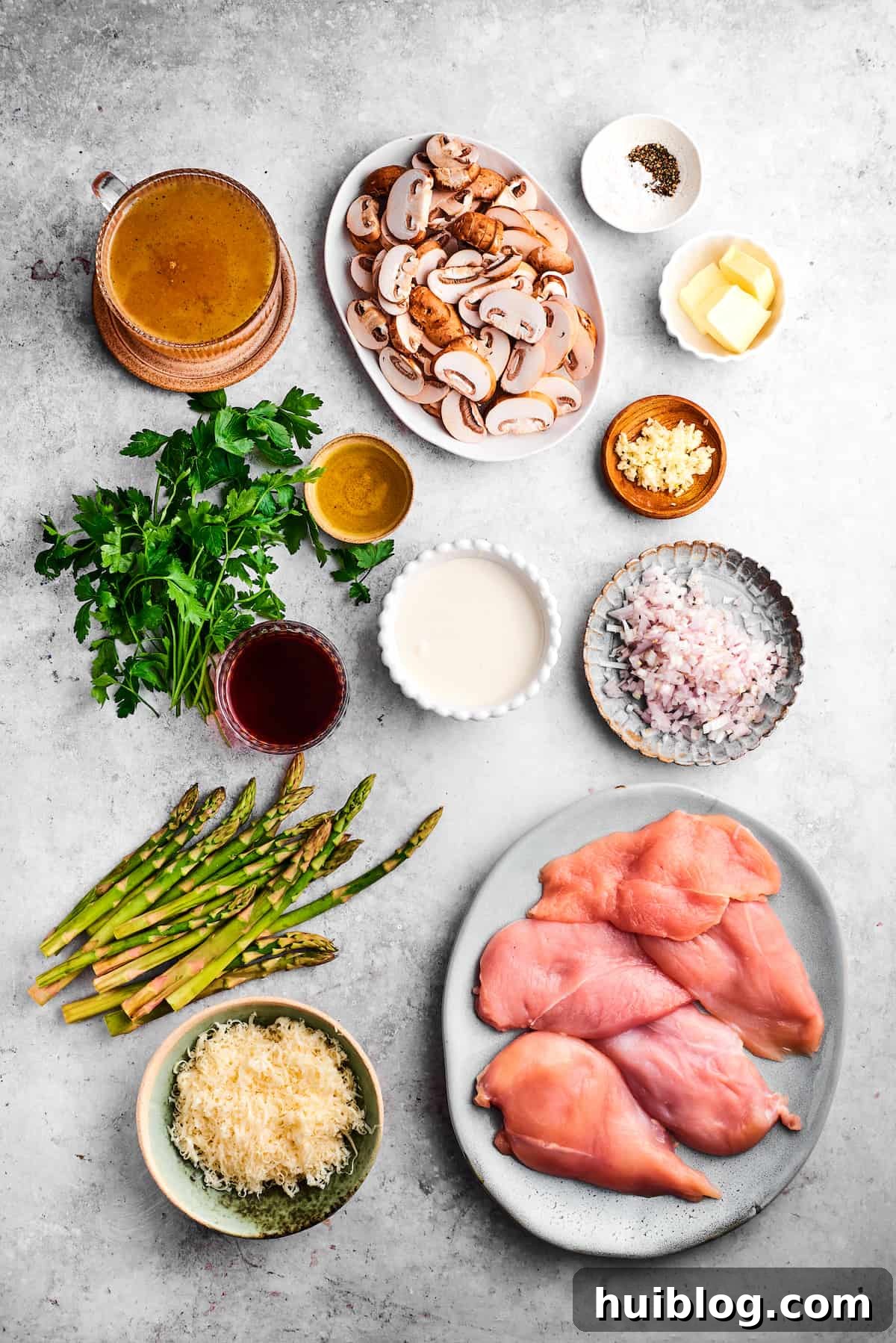 This creamy Chicken Madeira recipe is packed with savory sautéed mushrooms, sweet wine, tender chicken, and melted mozzarella cheese. The ingredients for chicken madeira are shown portioned out: chicken, mushrooms, asparagus, parsley, salt and pepper, butter, olive oil, madeira, garlic, mozzarella, cream, broth.
