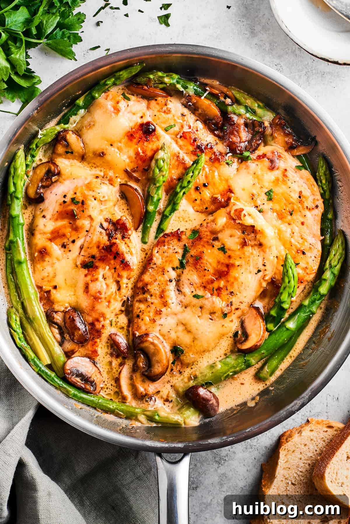 This creamy Chicken Madeira recipe is packed with savory sautéed mushrooms, sweet wine, tender chicken, and melted mozzarella cheese. Overhead image of Chicken Madeira in a skillet with asparagus spears and mushrooms.
