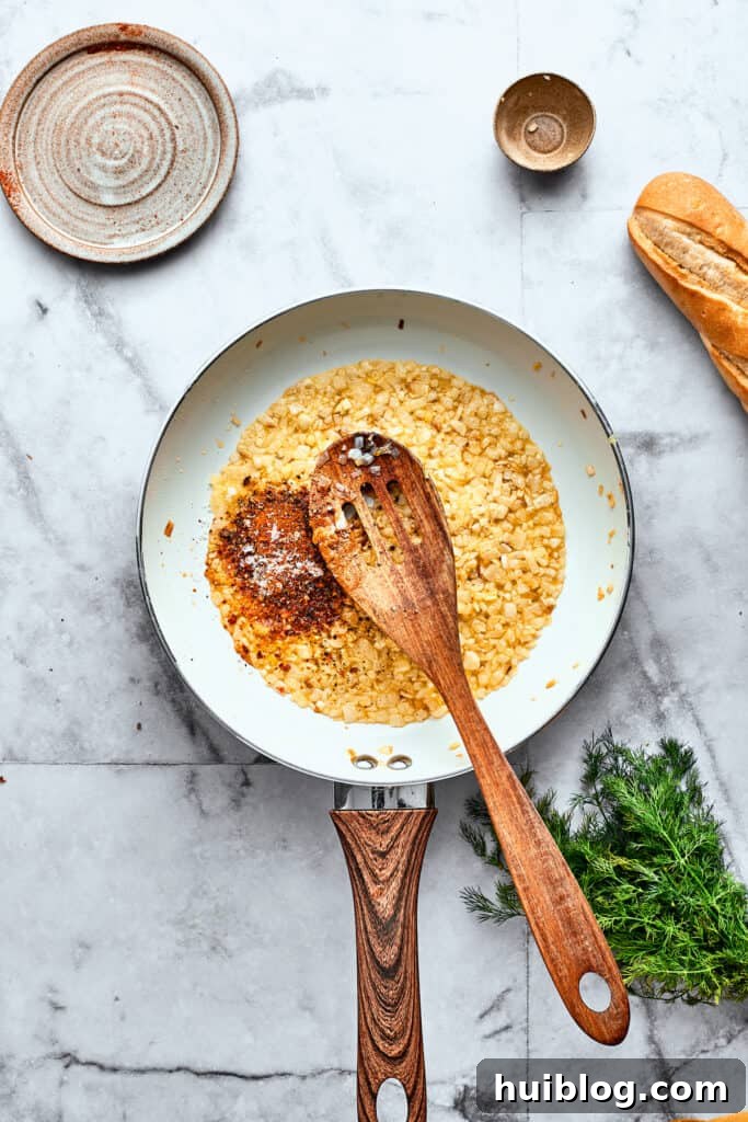 A wooden spoon stirs diced tomatoes into a skillet of onion and garlic.