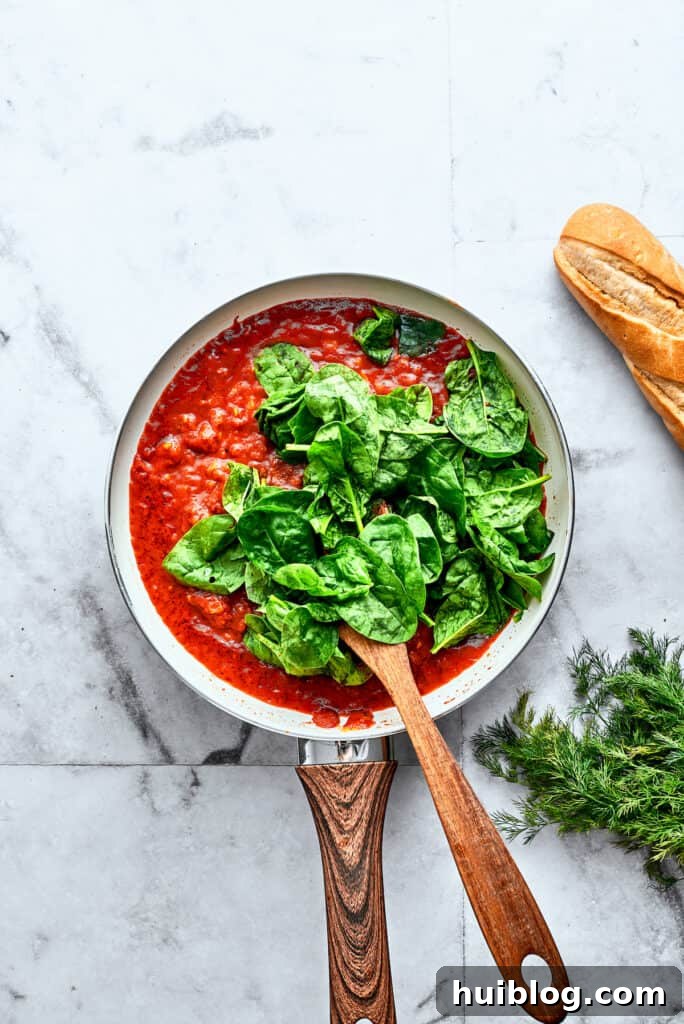 Bright green spinach leaves are stirred into a skillet of homemade tomato sauce.