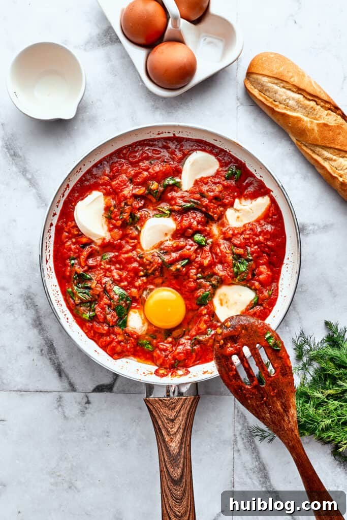 Eggs are added to a skillet of tomato sauce, spinach, and cheese.