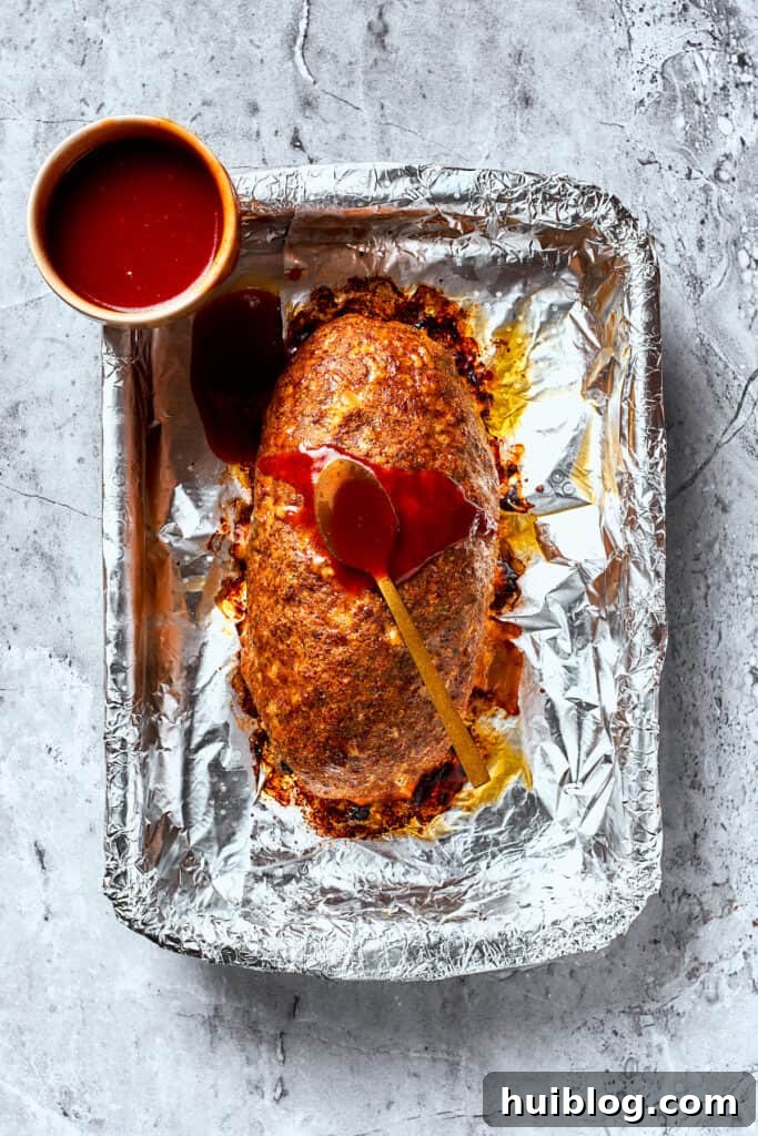 Comforting and hearty, Brown Sugar Meatloaf elevates ordinary meatloaf with a brown sugar-infused glaze for a hint of sweetness. The sweet brown sugar glaze is generously brushed over the partially baked meatloaf, still on its foil-lined pan, creating a glossy finish.