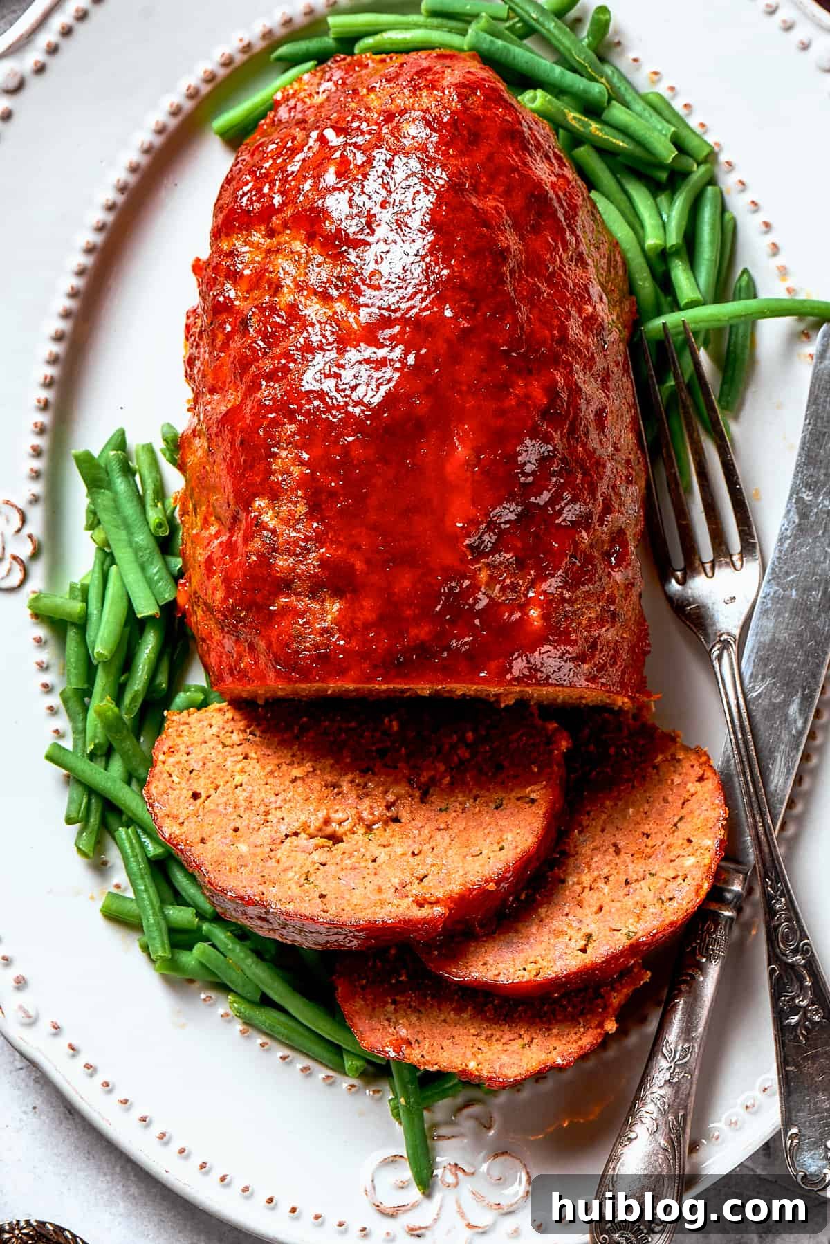 Comforting and hearty, Brown Sugar Meatloaf elevates ordinary meatloaf with a brown sugar-infused glaze for a hint of sweetness. An inviting overhead image of a whole brown sugar meatloaf, freshly glazed and garnished, presented on a rustic serving platter, ready to be sliced.