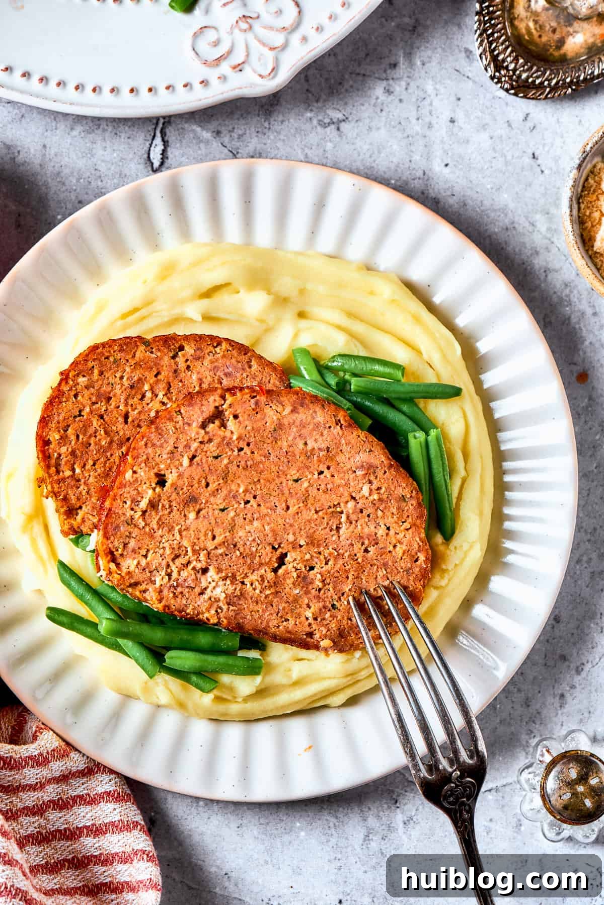 Comforting and hearty, Brown Sugar Meatloaf elevates ordinary meatloaf with a brown sugar-infused glaze for a hint of sweetness. Two generous slices of tender brown sugar meatloaf, beautifully glazed, served atop a creamy bed of mashed potatoes, ready for a comforting meal.