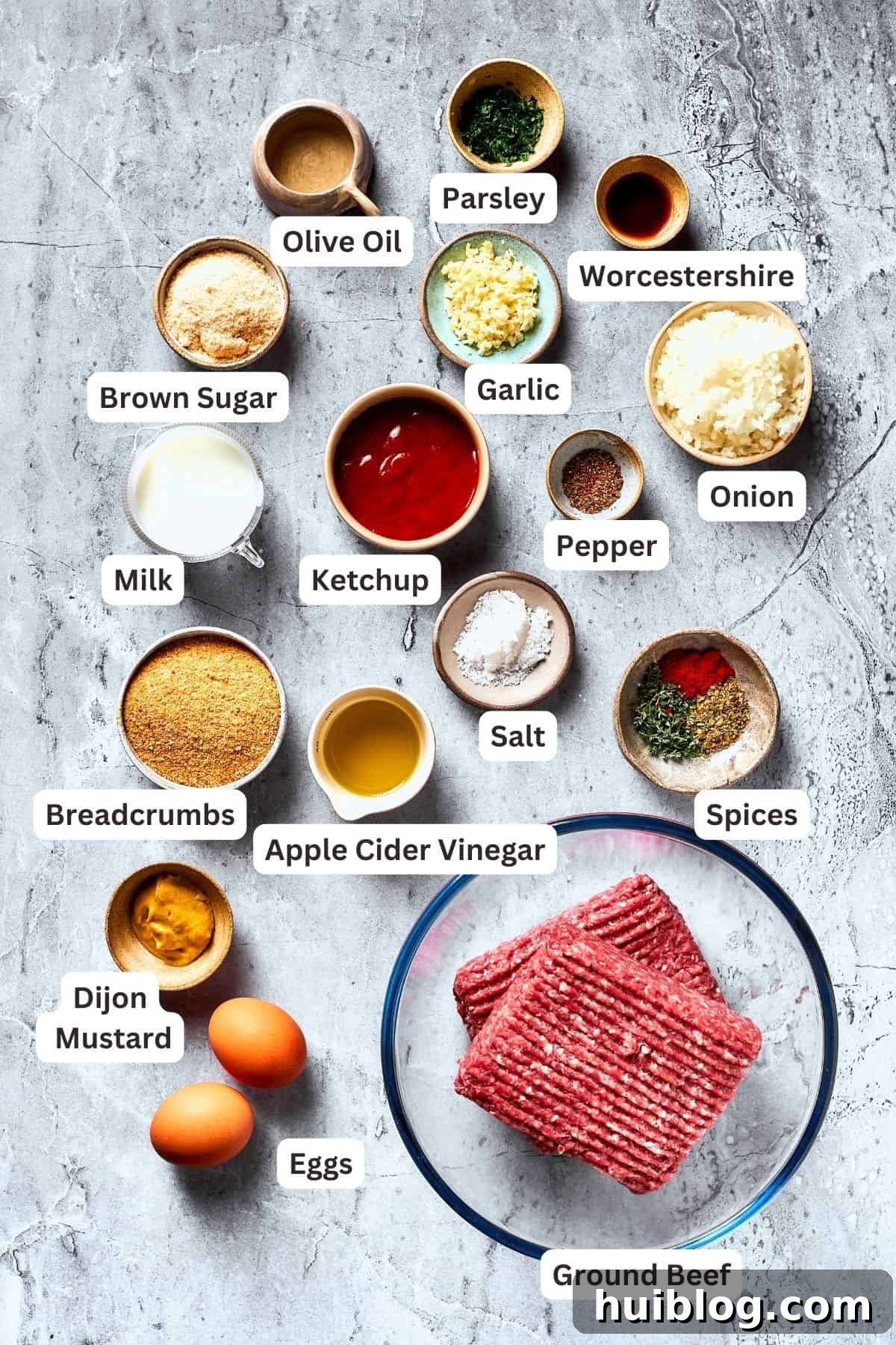 Comforting and hearty, Brown Sugar Meatloaf elevates ordinary meatloaf with a brown sugar-infused glaze for a hint of sweetness. The array of fresh and pantry ingredients for brown sugar meatloaf laid out and portioned, including ground beef, ketchup, brown sugar, apple cider vinegar, salt, pepper, dried herbs, onion, garlic, breadcrumbs, Worcestershire sauce, eggs, and olive oil.