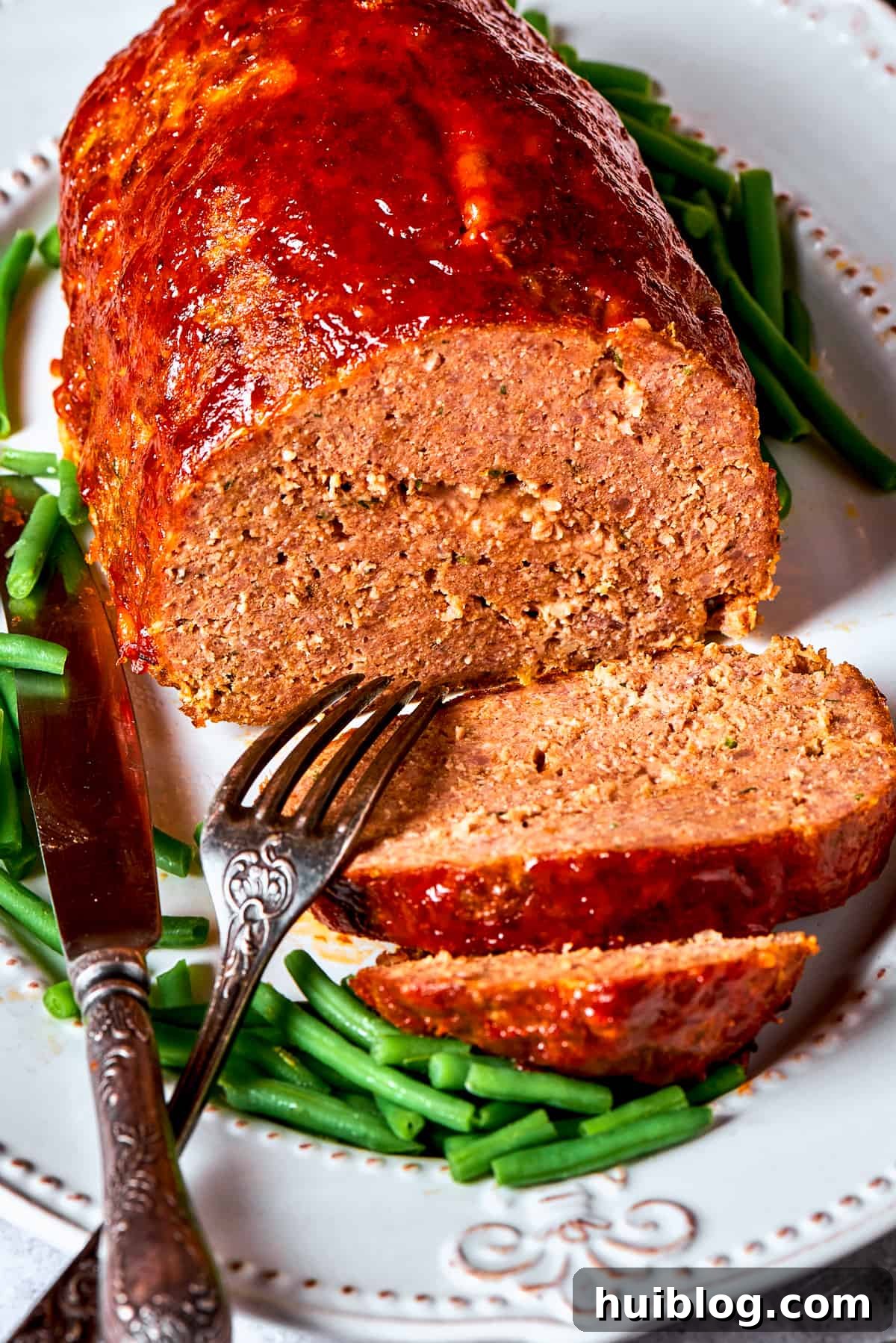 Comforting and hearty, Brown Sugar Meatloaf elevates ordinary meatloaf with a brown sugar-infused glaze for a hint of sweetness. A perfectly cooked brown sugar meatloaf, sliced to reveal its moist, flavorful interior and garnished with fresh herbs, served on a white platter.