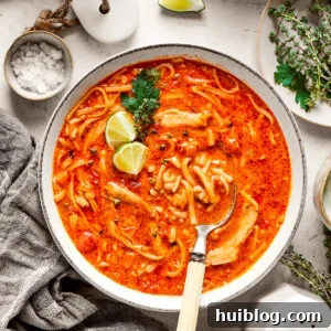 Two bowls of spicy chicken soup are shown with toppings arranged around them.