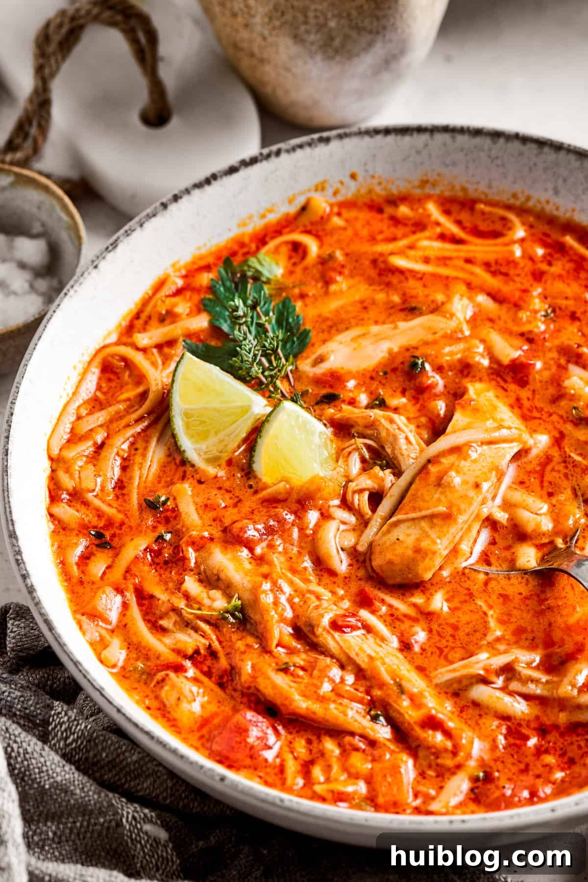 Close-up image of spicy chicken soup served in a bowl and garnished with lime wedges, ready to eat.
