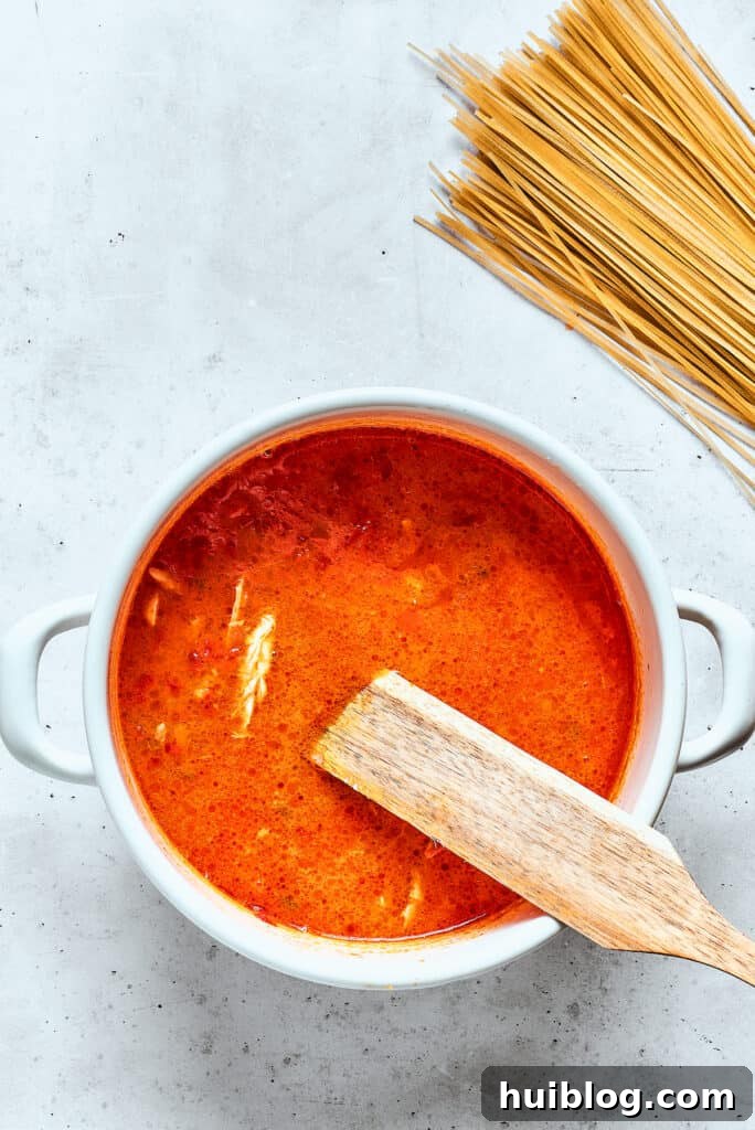 Noodles are added to spicy chicken soup with more noodles nearby, ready to be incorporated.
