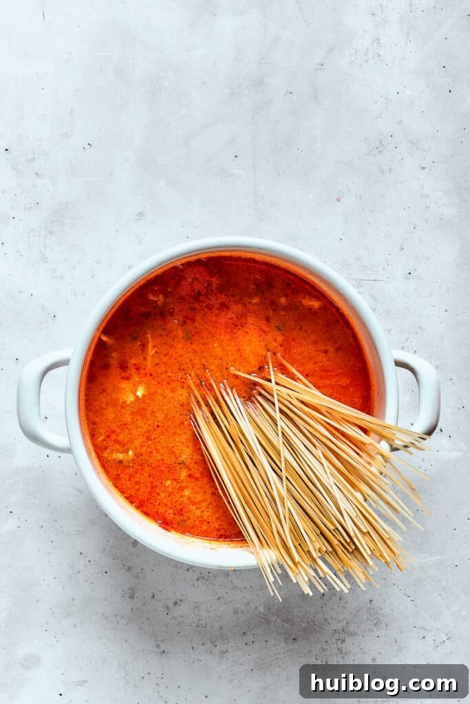 Rice noodles are added to a pot of spicy chicken soup, absorbing the rich flavors.