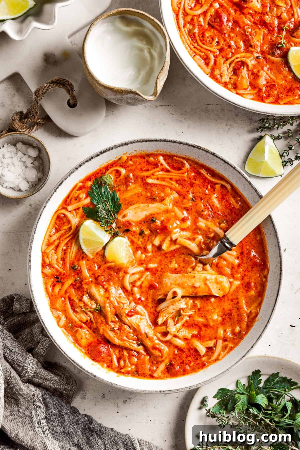 Two bowls of spicy chicken soup are shown with toppings arranged around them, garnished and ready to be enjoyed.